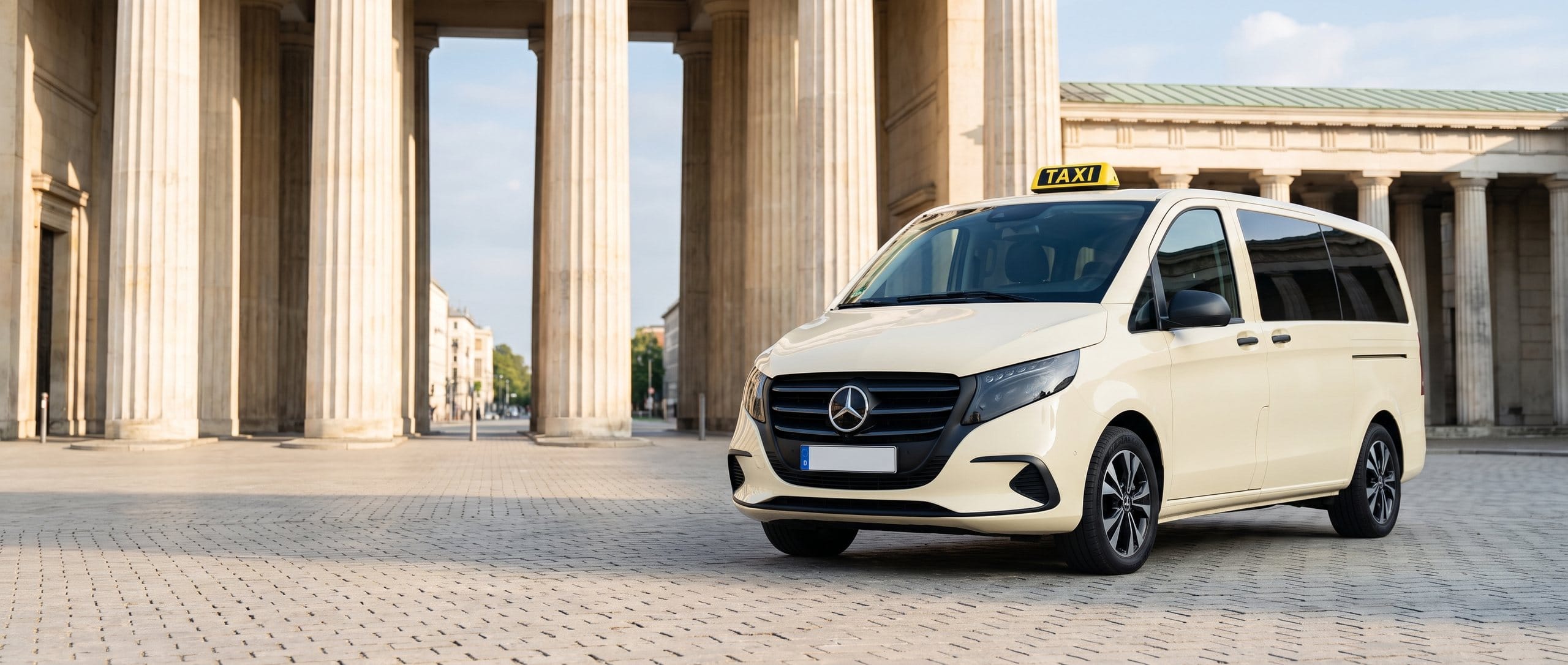 Elfenbeinfarbenes Großraumtaxi auf dem Pflaster des Münchner Königsplatzes vor den Säulen der Propyläen am Morgen